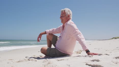 happy senior caucasian man sitting on the beach enjoying the view