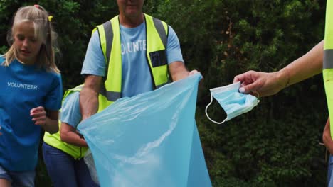 grupo de voluntarios de varias generaciones caucásicos recogiendo basura poniendo máscara facial en una bolsa