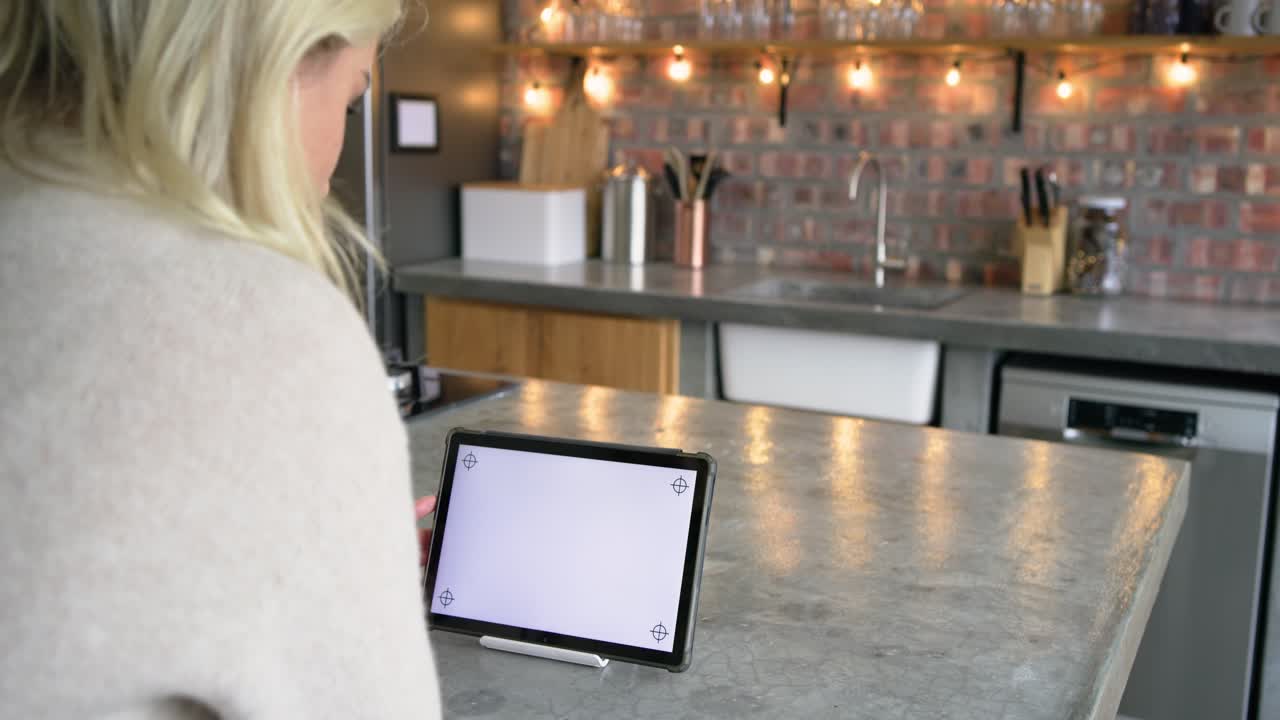 Woman entering kitchen, placing tablet on island, tapping screen, finishing selection while panning