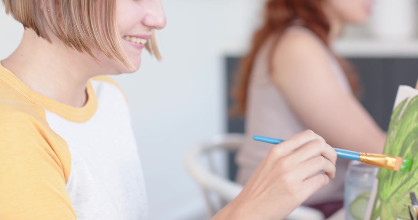 Amiche multietniche che iniziano a dipingere in studio, usando uno straccio per applicare il verde con un pennello blu sui cavalletti