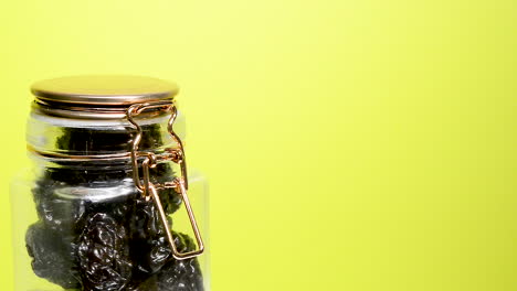 Detail-of-an-airtight-mason-jar-rotating-with-dried-plums-on-a-neon-yellow-background