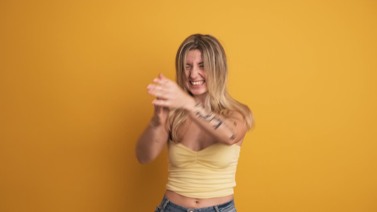 Smiling and jumping young woman with raised hands on yellow background