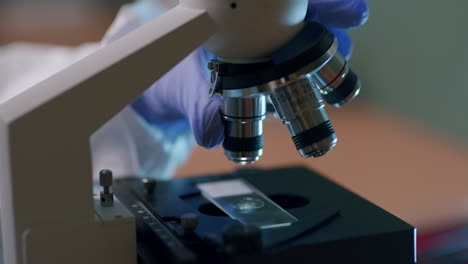 un joven científico de la vida cambia las lentes del microscopio profesional en el laboratorio: un primer plano de la torreta de la lente del microscopio