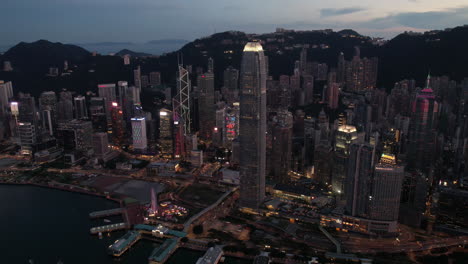 tiro de drone hiperlapso del centro de hong kong con rascacielos de iluminación y montañas en el fondo durante la hora azul