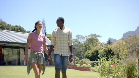 diverse couple holding hands and walking in garden, enjoying sunny day outdoors, copy space