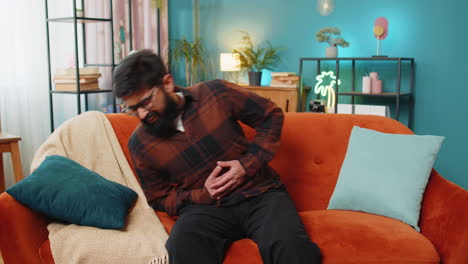 hombre indio molesto acostado en el sofá sintiendo repentina fuerte dolor abdominal dolor de estómago problema de gastritis