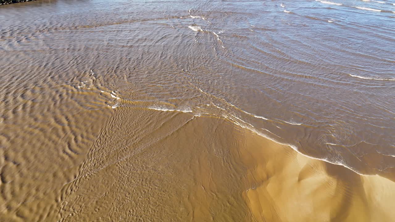 Clear shallow seawater flows over rippled sandbank in sunlight at Nambucca Heads, Australia
