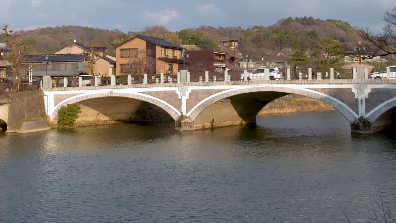 Static wide shot of a stone arch bridge over a river under cloudy skies