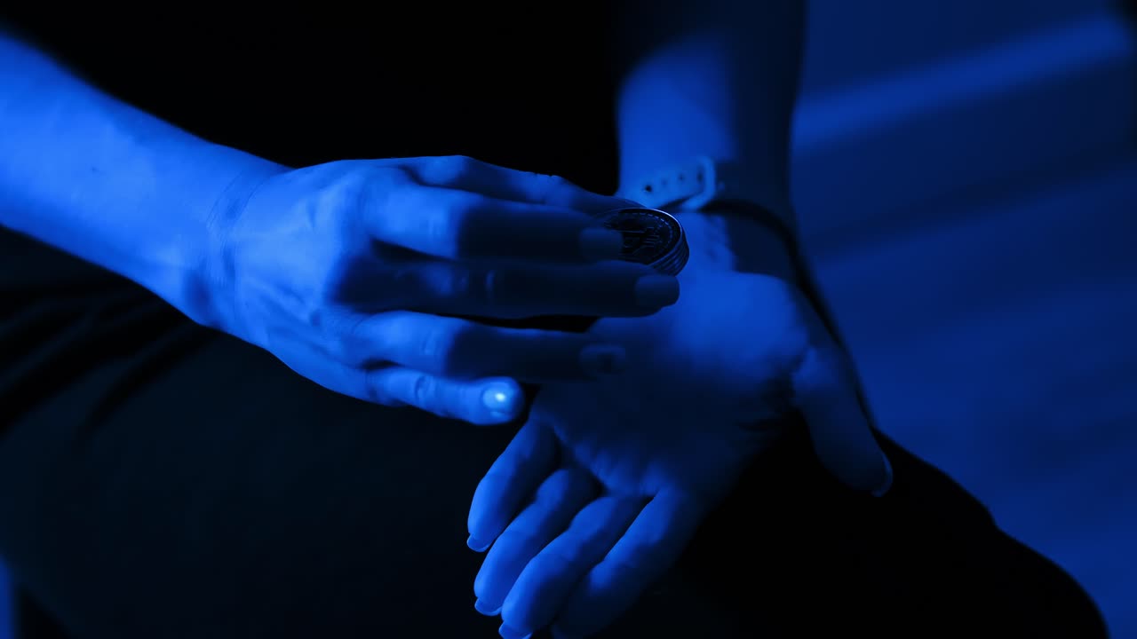 Cryptocurrency coins drop between hands in blue tone symbolizing doubt