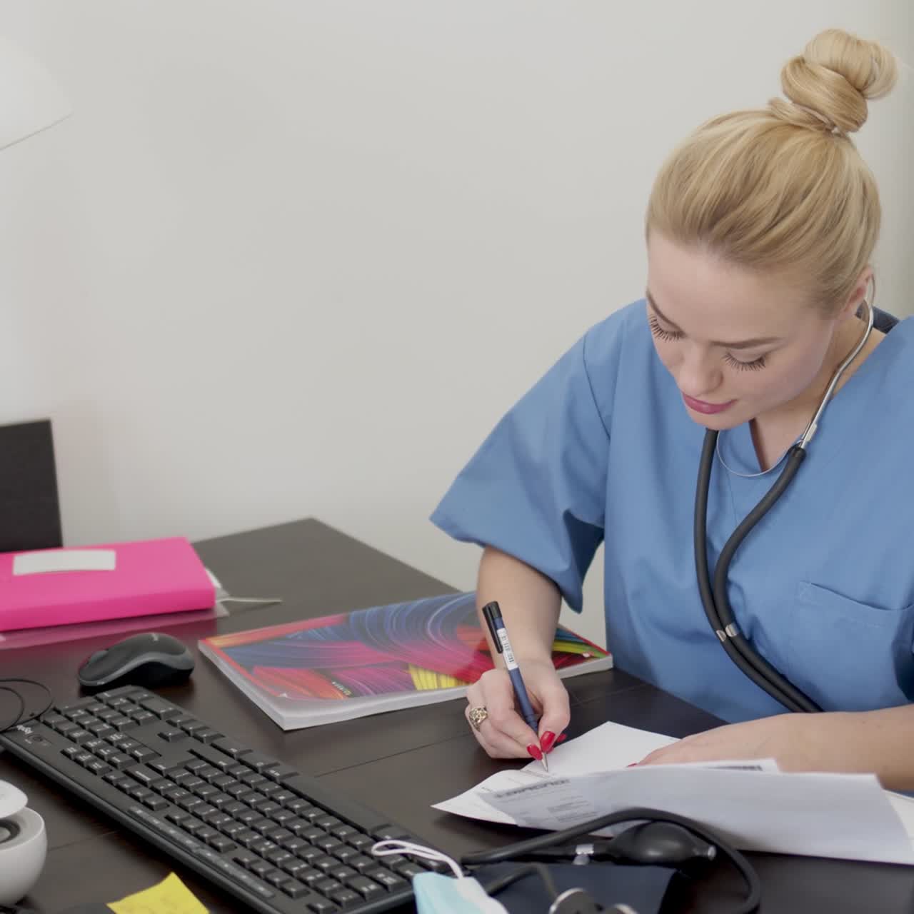 joven y hermosa doctora rubia con abrigo azul trabajando en el escritorio usando una computadora y haciendo papeleo