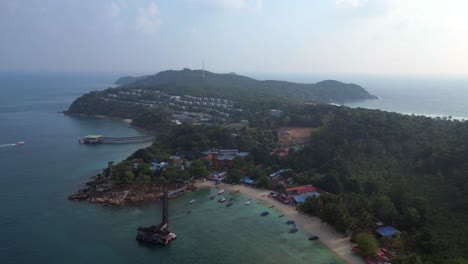 Morning-mood-Dramatic-aerial-view-flight-speed-ramp-of-a-tropical-island-with-a-long-wooden-pier-leading-to-a-floating-restaurant,-surrounded-by-turquoise-waters-and-lush-green-rainforest