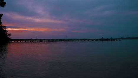 Gentle-ocean-waves-caress-the-lonely-beach-in-Koh-Chang,-Thailand,-while-the-sky-is-ablaze-with-the-warm-hues-of-a-breathtaking-sunset-–-a-vivid-canvas-of-orange,-purple,-and-red