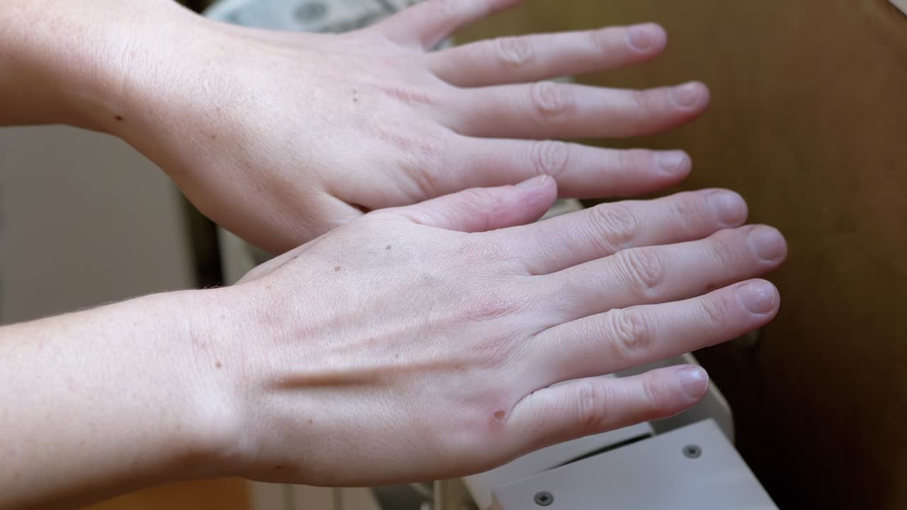 한 여성이 방에서 집에서 배터리에 손을 따뜻하게합니다. 4k. 근접. 느린 모션