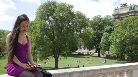 Asian-Woman-Sitting-in-front-of-Burggarten-in-Vienna,-reading---Slow-Motion