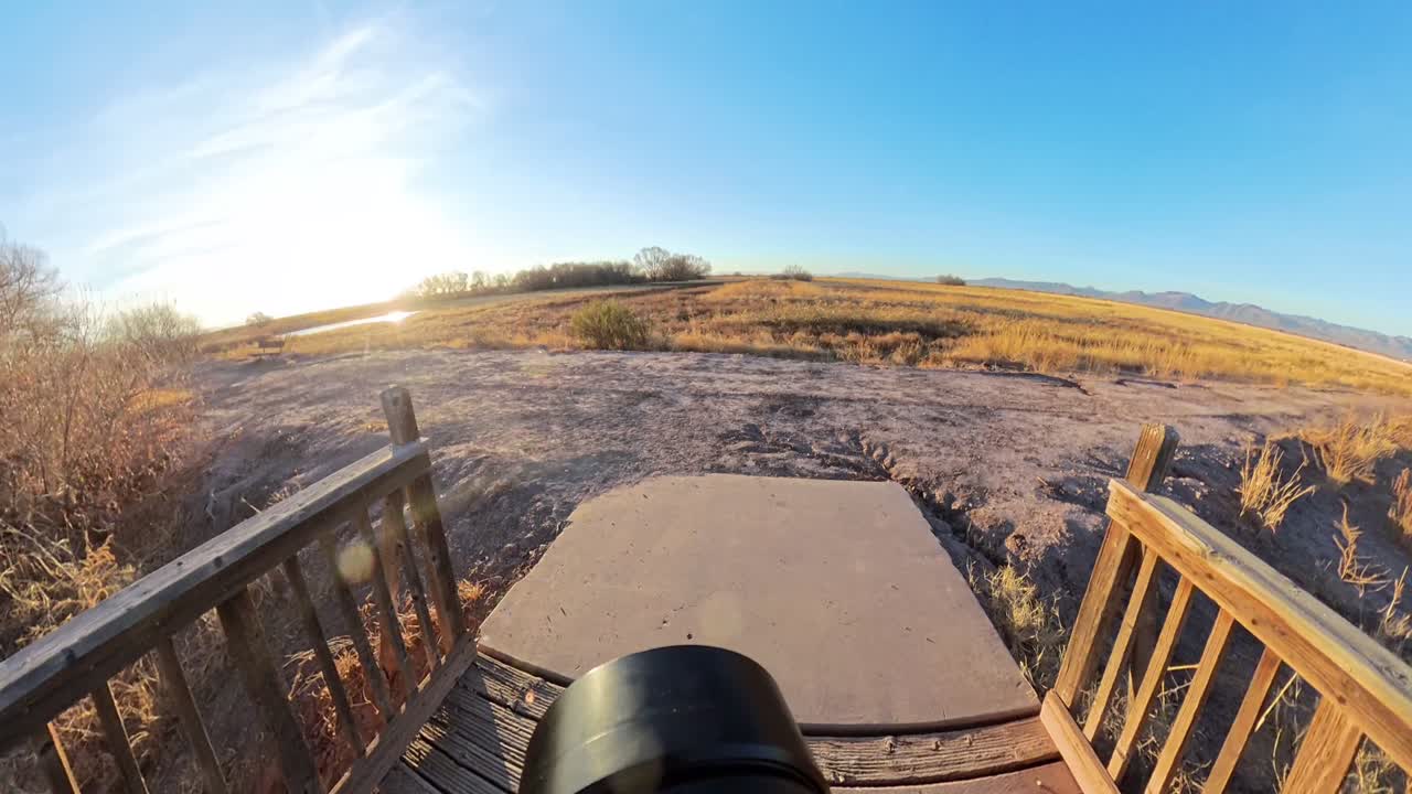 Lens view of a photographer walking down a wooden deck to dry Arizona Grassland.
