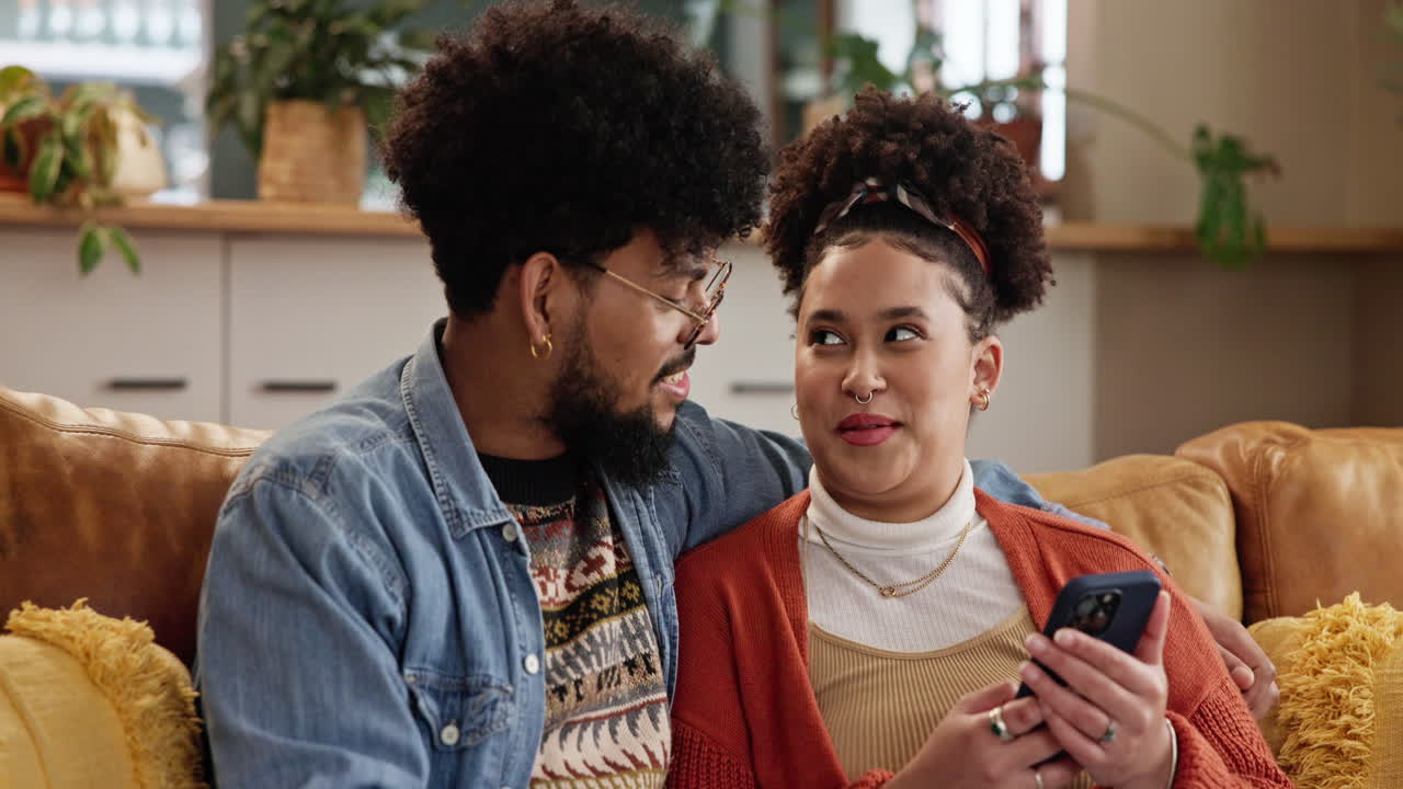 pareja sentada en un sofá y riendo juntos mientras miran un teléfono