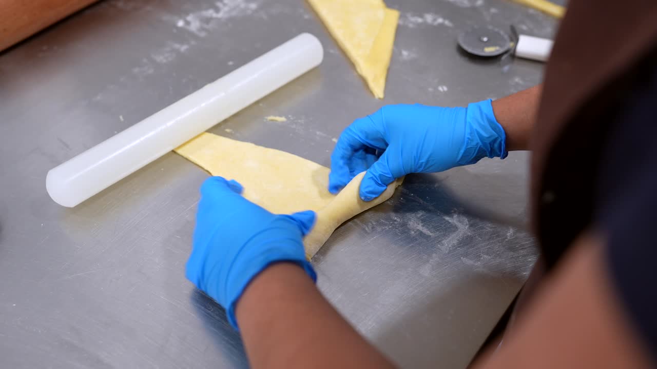 Baker's Hands in Blue Gloves Shaping Dough for Croissants