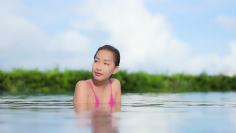 Mientras-Disfruta-Del-Agua-En-Una-Piscina-Rodeada-De-Vegetación-Tropical,-Vuelve-Los-Ojos-A-La-Cámara-Y-Sonríe