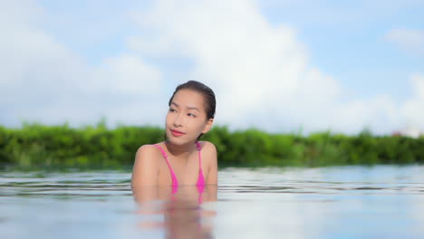 mientras disfruta del agua en una piscina rodeada de vegetación tropical, vuelve los ojos a la cámara y sonríe