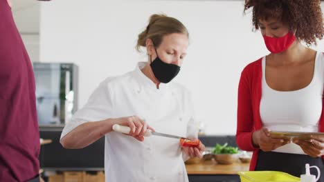 cocinera caucásica que enseña a un grupo diverso usando máscaras faciales