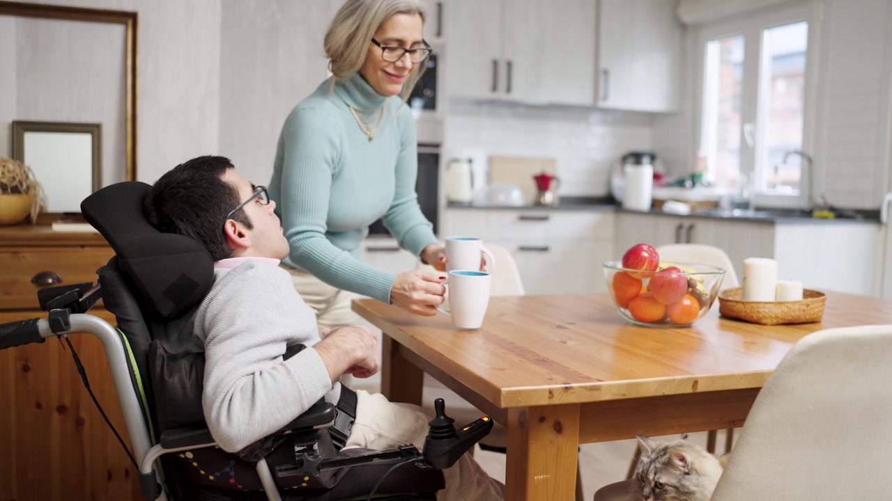 Assistente che serve il caffè a un giovane in sedia a rotelle a casa.
