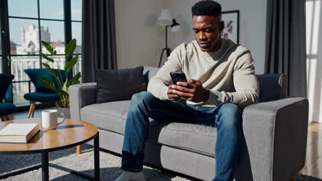 a man sitting on a sofa and using his smartphone in a modern living room