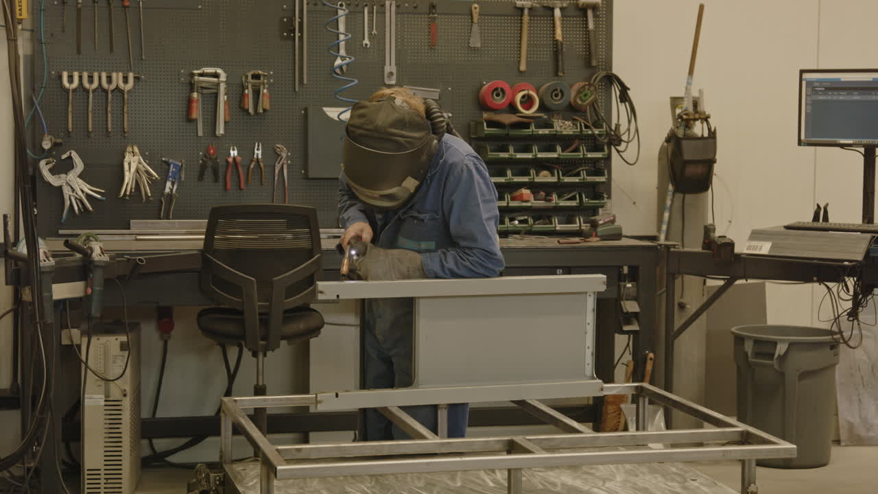 A welder in safety gear uses a torch to weld a piece of metal in a workshop