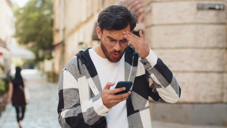 arabian young man using smartphone loses becoming surprised sudden lottery result standing on street