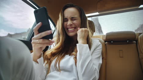 portrait of happy business lady getting good news on video call in business car.