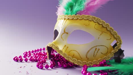 Video-of-carnival-masquerade-mask-with-feathers-and-pink-mardi-gras-beads,-on-purple-background