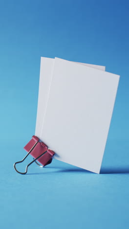 vertical video of blank white business cards with bulldog clip on blue background, copy space