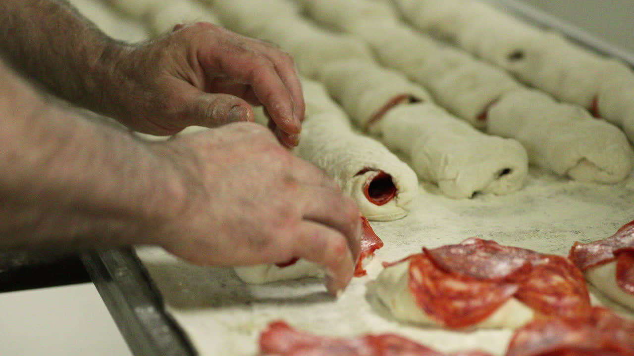 Mani di fornaio che stendono l'impasto con fette di prosciutto - Rotolo di pane al prosciutto - primo piano