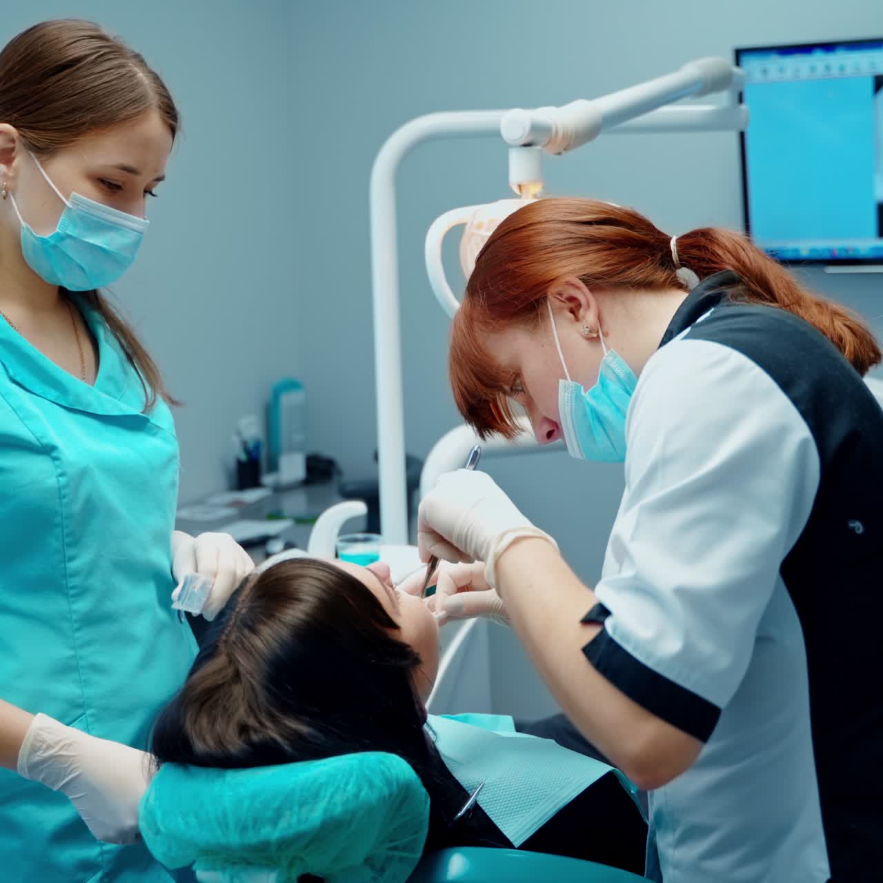 Dental procedure in stomatology cabinet. Patient sitting in dental chair while professional dentist and a nurse treating teeth.