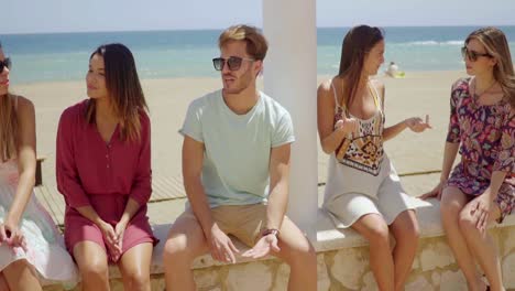 Six-young-students-sitting-chatting-on-a-wall