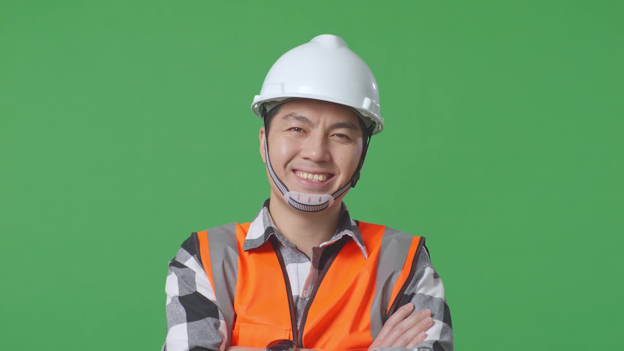 Close Up Of Asian Male Engineer With Safety Helmet Crossing His Arms And Smiling To Camera While Standing In The Green Screen Background Studio