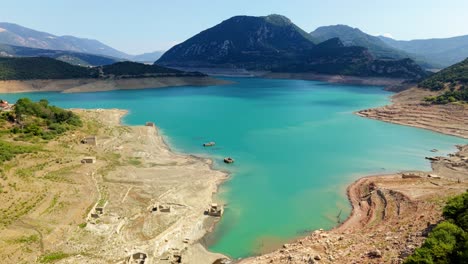 drone glides over turquoise reservoir bordered by forest and dry ground near greek hills
