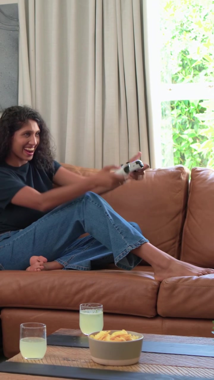 Video verticale: Donna in maglietta scura che reagisce all'inizio di un gioco, giocando con un controller bianco a casa.