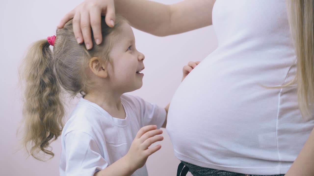 예쁜 소녀가 임신 중인 엄마와 이야기하고 방에서 배를 만지고 있습니다.