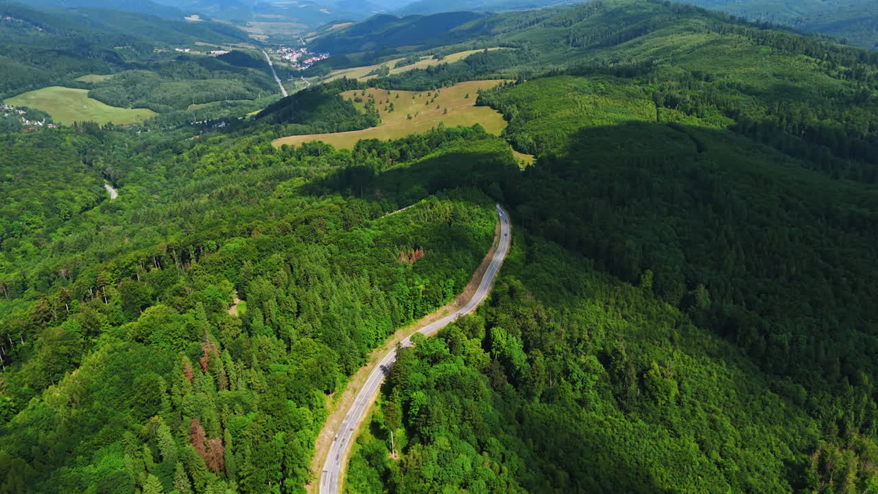 Winding forest road aerial view. A winding road cuts through lush green forests in a mountainous landscape on a sunny day