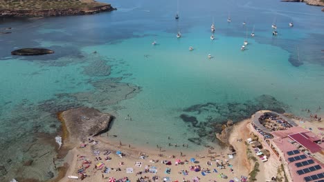 drone footage over the beach of cala escondida on the island of ibiza and the marina where many boats are anchored