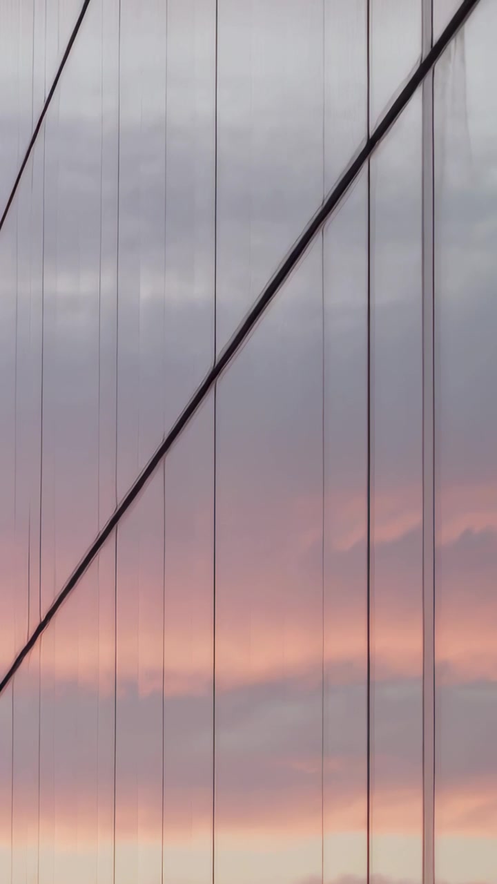 Video verticale: Telecamera che panoramica, mostrando un cavo diagonale e appendini verticali al crepuscolo, con un cielo rosa.