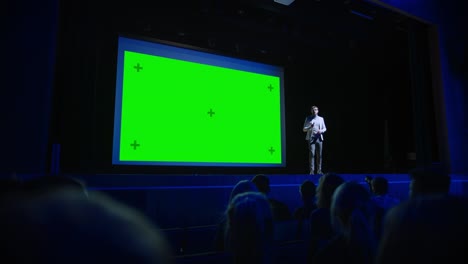 software startup founder does presentation of new product to the audience, behind him movie theater with green screen, mock-up, chroma key. business conference live event or device reveal