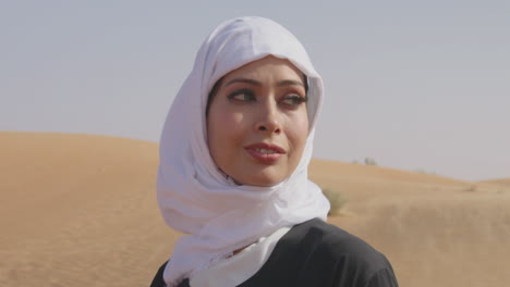 ritratto di una bella donna musulmana in hijab bianco e abito nero tradizionale in piedi in un deserto ventoso e sorridente alla telecamera 2