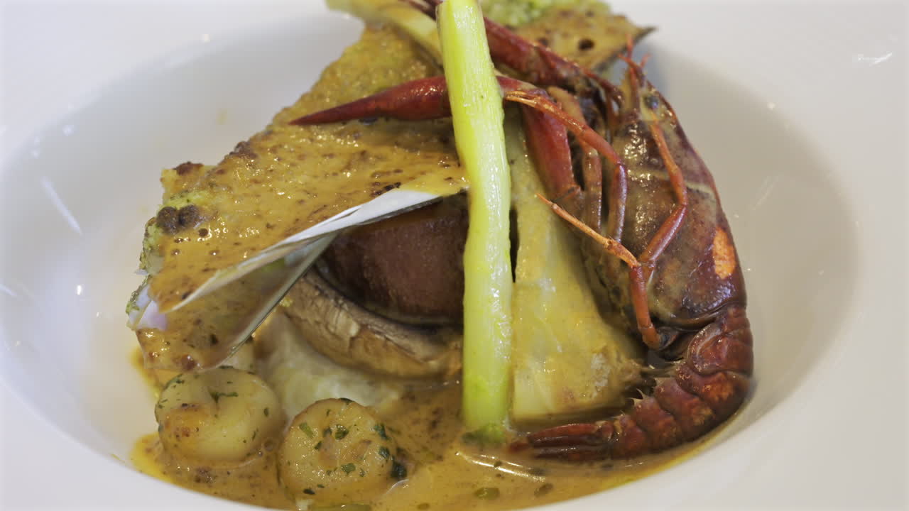 Close up of whole cooked crayfish with a mussel shell filled and a creamy herb topping on a white plate
