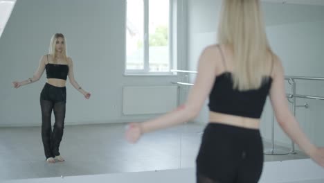 fit girl in black clothes performing contemporary. female dancer shows flowing motions, body and hands waves at white room. modern ballet dance choreography. young woman is moving smoothly