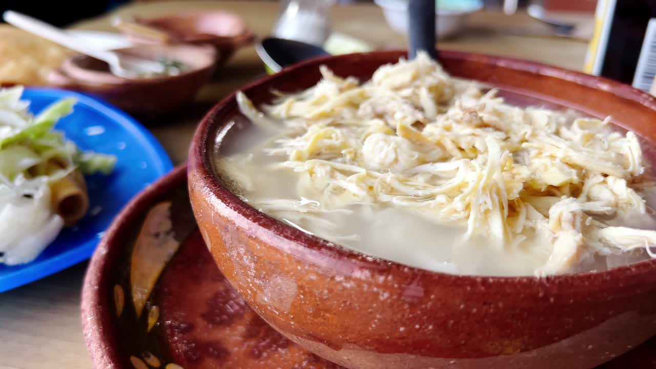 A warm bowl of pozole soup with shredded chicken in a traditional ceramic dish