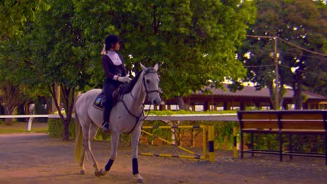 Cinematic-slow-motion-shot-of-a-beautiful-woman-riding-a-white-horse-while-wearing-a-black-and-white-outfit-with-matching-white-gloves-and-black-boots-on-a-sunny-day,-Slomo