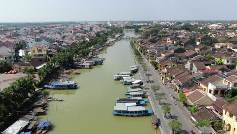 drone aerial view in vietnam flying over hoi an brown color river canal in the city, small brick houses and wooden boats on a sunny day