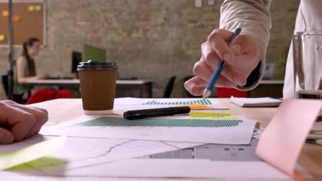 business team holding meeting in modern office, everyone standing behind table with papers and planning, pointing on documents