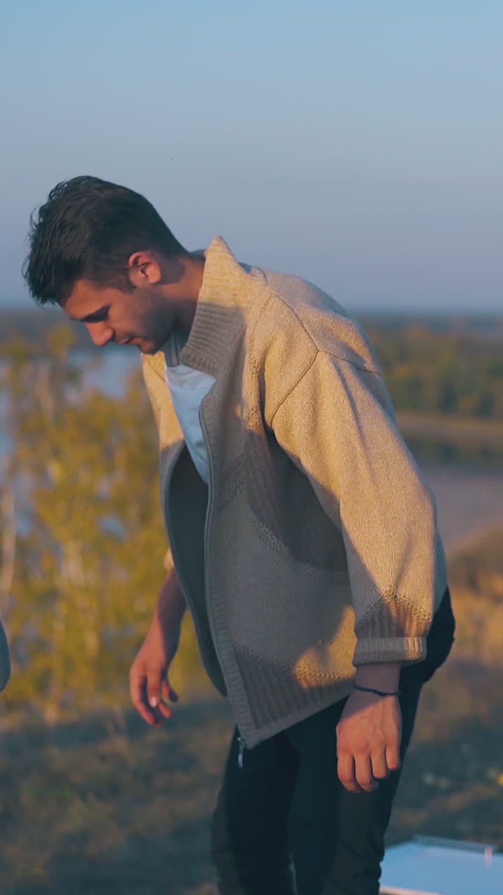 beautiful young couple guy girl spend time in camp on steep bank against calm wide river and blue sky in autumn evening
